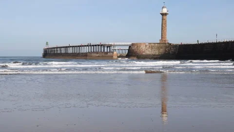 Rolling waves with Whitby Harbour Pier reflected in the wet sand on Whitby Beach Stockbeeldmateriaal 247624380