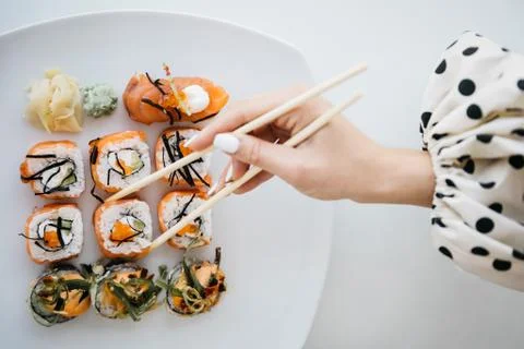Rolls and sushi on a white plate. Hand with sushi sticks. Stock Photos