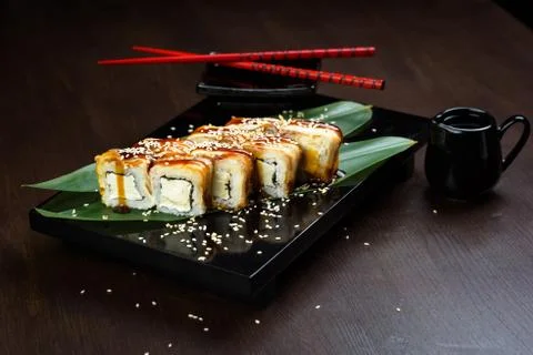Rolls with eel and cheese on the board with sauce and red chopsticks Stock Photos
