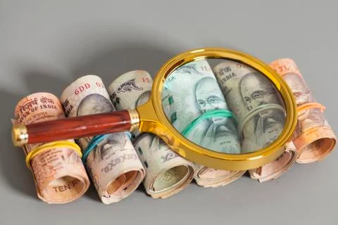 Rolls of Indian Currency Rupee Notes with magnifying glass on gray Foto stock