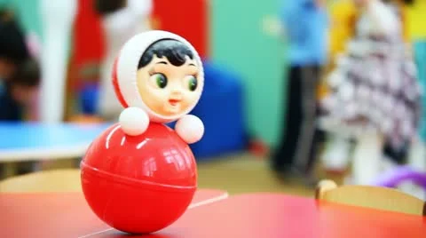 Roly-poly toy wobbles on table, in defocus behind it children play Stock Footage 10857037