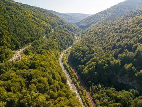 Romanian mountain valley extends between forested slopes, with river, railway Foto stock
