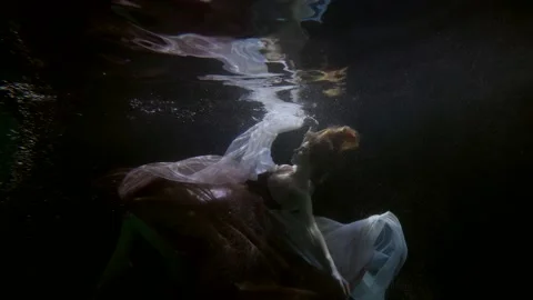 Romantic and dramatic underwater shot with graceful woman diving in depth of sea 動画素材 168132283