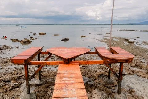 Romantic beach dining setup featuring a wooden heart shaped table and seating Stock Photos