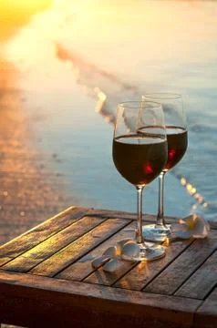 Romantic beach scene: two glasses of red wine at sunset near water Stock Photos