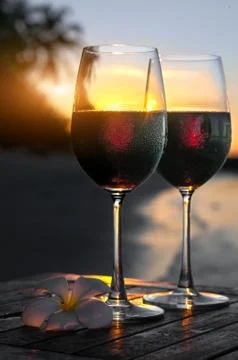 Romantic beach scene: two glasses of red wine at sunset near water Stock Photos