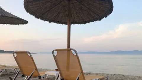 Romantic beachfront view of two orange sunbeds at twilight under straw Stock Footage 135048897