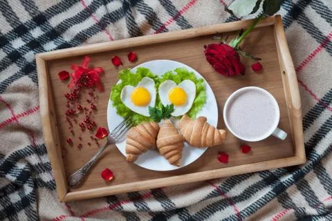 Romantic breakfast in bed with heart-shaped eggs, jam toasts, croissants, rose Stock Photos