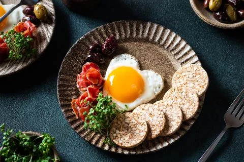 Romantic breakfast - fried eggs in the shape of a heart and olives. Healthy b Stock Photos