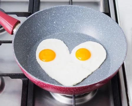Romantic breakfast - scrambled eggs in the form of a heart on a red frying pa Stock Photos
