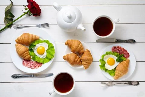 Romantic breakfast for two with heart shaped eggs, salad, croissants, rose Stock Photos