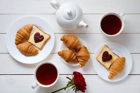Romantic breakfast for two with toasts, heart shaped jam, croissants, rose and Stock Photos