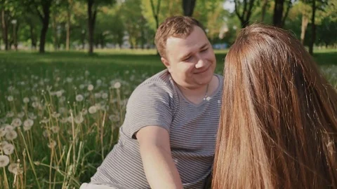 Romantic couple among white dandelions in the clearing. They look at each other Stock Footage
