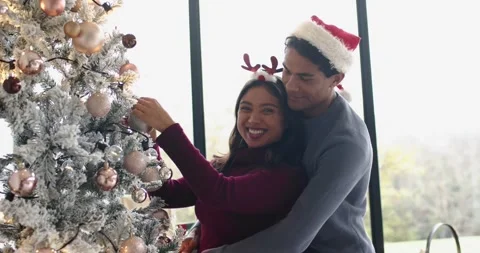 Romantic couple decorating Christmas tree selecting and hanging bauble beside Stock Footage 342926962