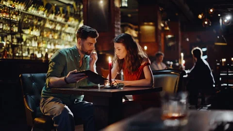 Romantic couple discussing menu sitting cozy bar interior with glowing candle. Stock Footage 334003848
