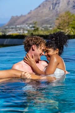 Romantic couple embracing in infinity pool, laughing with sunglasses and striped Stock Photos