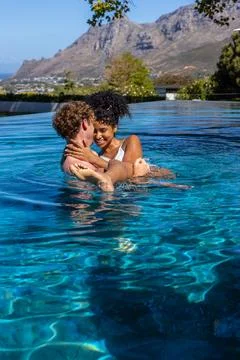 Romantic couple embracing in infinity pool near edge, white swimsuit, Foto stock