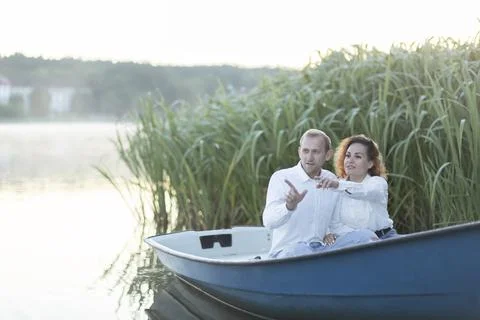 Romantic couple enjoys time sitting in boat, sailing in water,pointing fingers Stock Photos