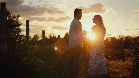 Romantic couple with glasses of wine at sunset. They look at each other, stand Видео 98301289