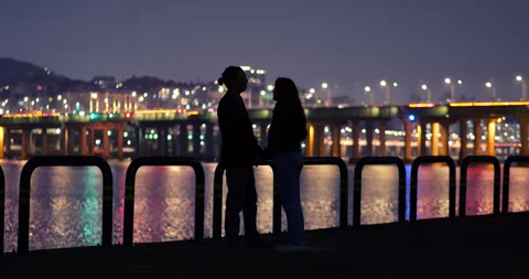 Romantic couple holding hands, talking by Han River in Seoul at night Stock Footage 303990866