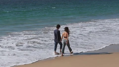 Romantic Couple Holding Hands While Walking Barefoot On Sandy Shoreline 動画素材 310955057