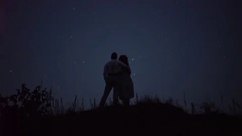 A romantic couple in the mountains embrace each other, with stars on a 스톡 동영상 80207327
