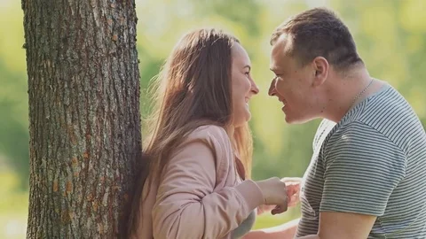A romantic couple near a tree in the park laughs, tickles each other in embrace Stock Footage