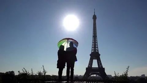 Romantic couple protected  by colored umbrella close Eiffel tower, sun shinning Stock Footage 69181885