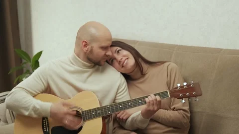 A romantic couple in a relationship are sitting on the couch and playing guitar Video stock 241185448