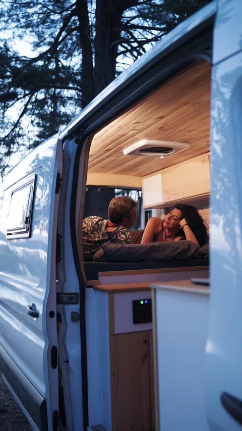 Romantic couple relaxing on bed in camper van at dusk. Vertical Stock Footage 344824457