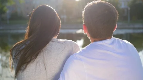 Romantic couple sat on the green grass near the pond. Back view. Couple Trust Video stock 116688341
