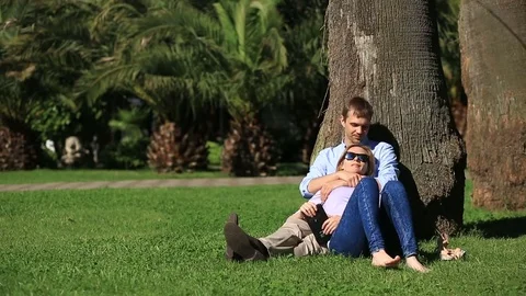 Romantic couple sitting under a palm tree. A girl on the lap of a guy. A loving Stock Footage 75603835