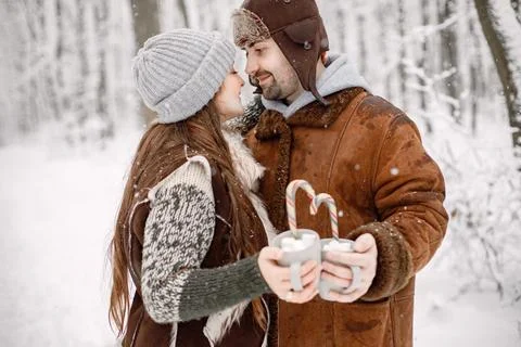 Romantic couple standing in winter forest, hugging and holding two cups with Stock Photos