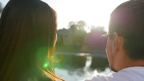 Romantic couple talking and sitting on the green grass near the pond on sunset Stock Footage 116693514