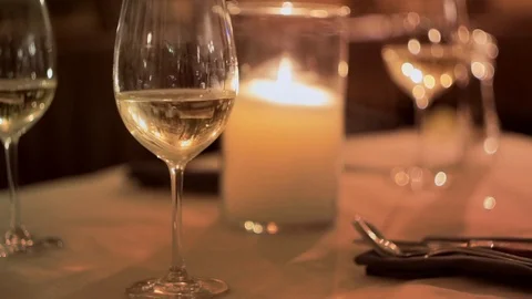 Romantic dinner: burning candle and glasses with white wine on restaurant table. Vídeo Stock 107777805