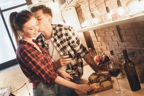 Romantic dinner concept. Cheeses and wine, husband kisses his wife Stock Photos