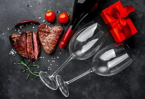 Romantic dinner setting with steak wine glasses and gift Stock Photos