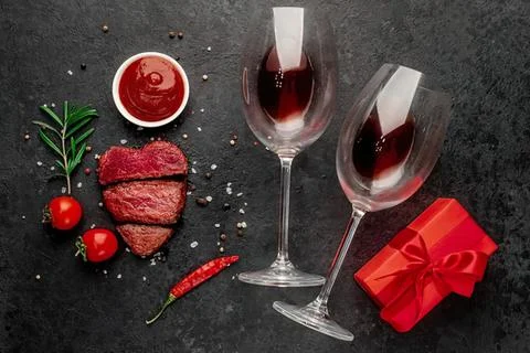 Romantic dinner setting with wine glasses, steak, and gift Stock Photos