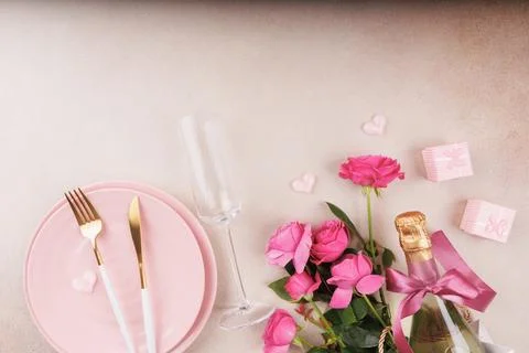 Romantic dinner setup with pink plates, champagne, and fresh roses Foto stock