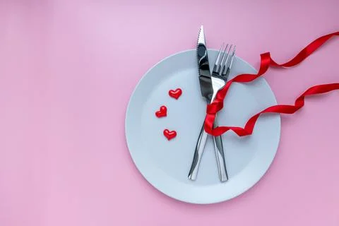 Romantic dinner table. plate, fork and knives with ribbon on pink background. Stock Photos