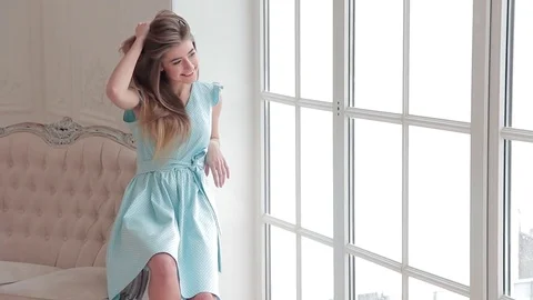 Romantic fashion model posing siting on sofa near window in light blue dress Stock Footage 72658990