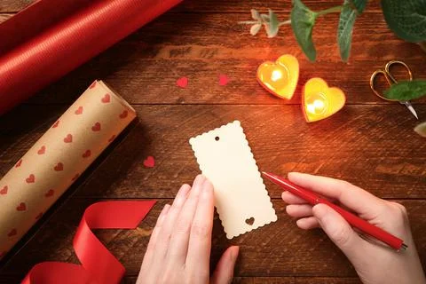 Romantic flat lay with hands writing gift tag on wooden table. Heart candle.. Stock Photos