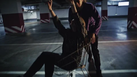Romantic Fun: Boyfriend Pushing Girlfriend in Shopping Cart in Parking Area 库存影片 332535341