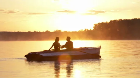 Romantic golden river sunset. Loving couple on small boat backlit by sunlight Stock Footage
