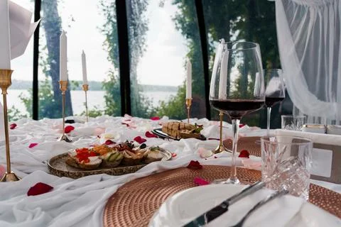 Romantic Lakeside Dinner Setup with Wine, Rose Petals, and Appetizers in a Glass Stock Photos