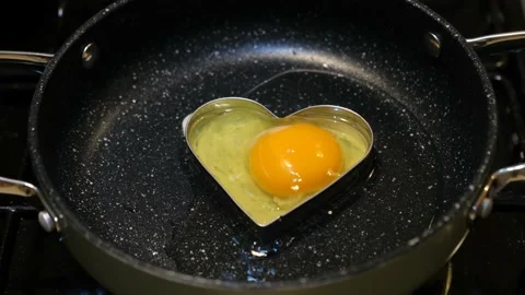 Romantic man cooking an egg with a heart for breakfast on Valentine's Day. Stock Footage