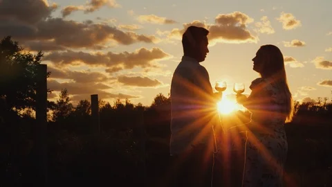 Romantic multi-ethnic couple drinking wine at sunset. They stand near the Stock Footage 98294549