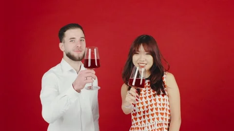 A romantic multiracial couple drinks wine together against a red background, cel Stock-Footage 296394991