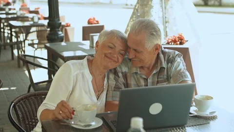 Romantic old couple with cups of tea looking at laptop sitting in a summer cafe Stock Footage 199385328