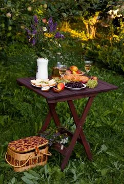 Romantic picnic setup featuring wine, cheese, and fruits in orchard setting Stock Photos